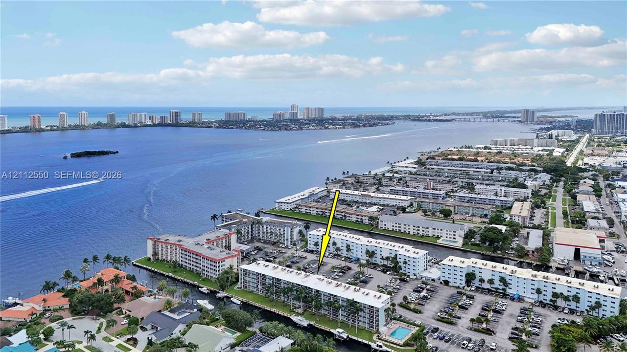 Aerial perspective featuring a multi-story residential building located along a waterfront canal with proximity to the coastline