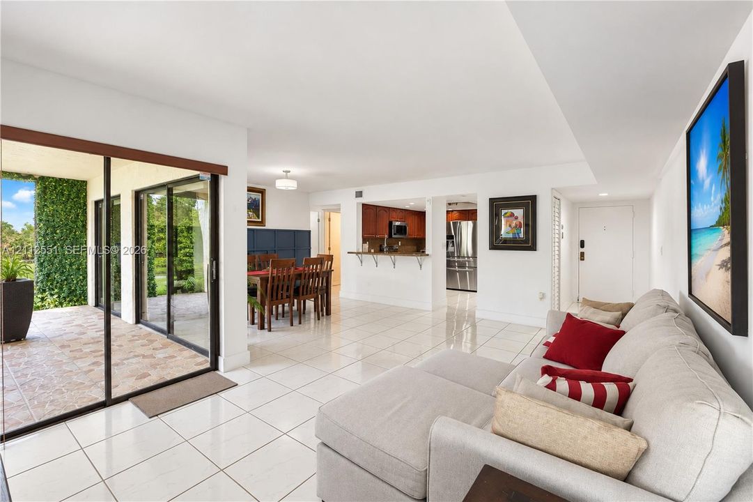 Open-concept living space featuring high-gloss tile flooring, sliding glass door access to a covered patio, and a kitchen pass-through counter