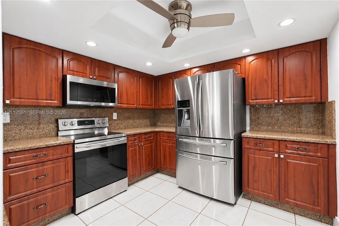 Kitchen featuring cherry-finish cabinetry, stone countertops, stainless steel appliances, a recessed ceiling with a central fan, and tile flooring