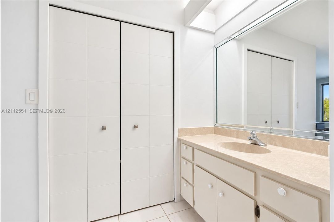 Built-in storage featuring double-door closets, vanity with stone-finish countertop, integrated oval sink, and large wall-mounted mirror