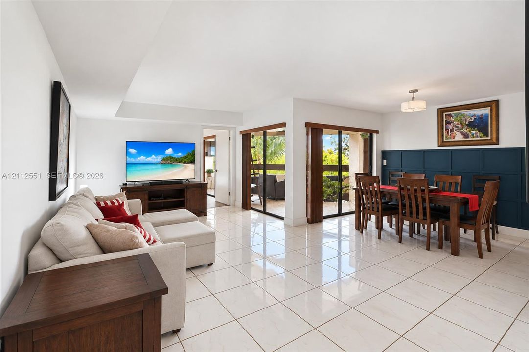 Open-concept living and dining area featuring polished tile flooring, dark blue wall paneling, and dual sliding glass doors providing outdoor access