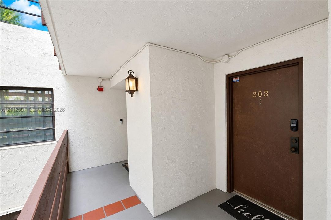Entrance featuring a textured white stucco facade, solid-tone entry door with electronic deadbolt, wall-mounted coach lantern, and tiled landing