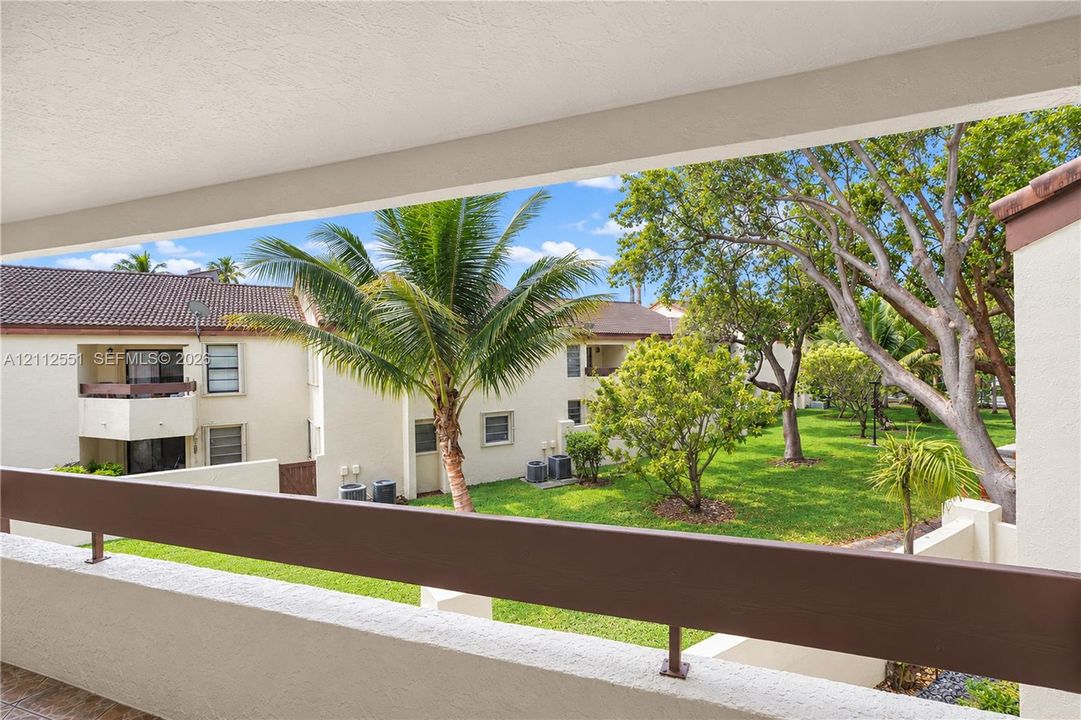 Covered balcony featuring a horizontal railing and expansive outdoor grounds with mature trees and manicured lawn