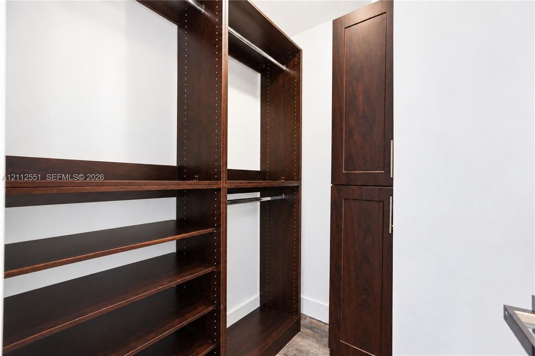 Built-in dark wood-finish cabinetry featuring adjustable shelving, integrated hanging rods, and full-height cabinetry with metallic hardware