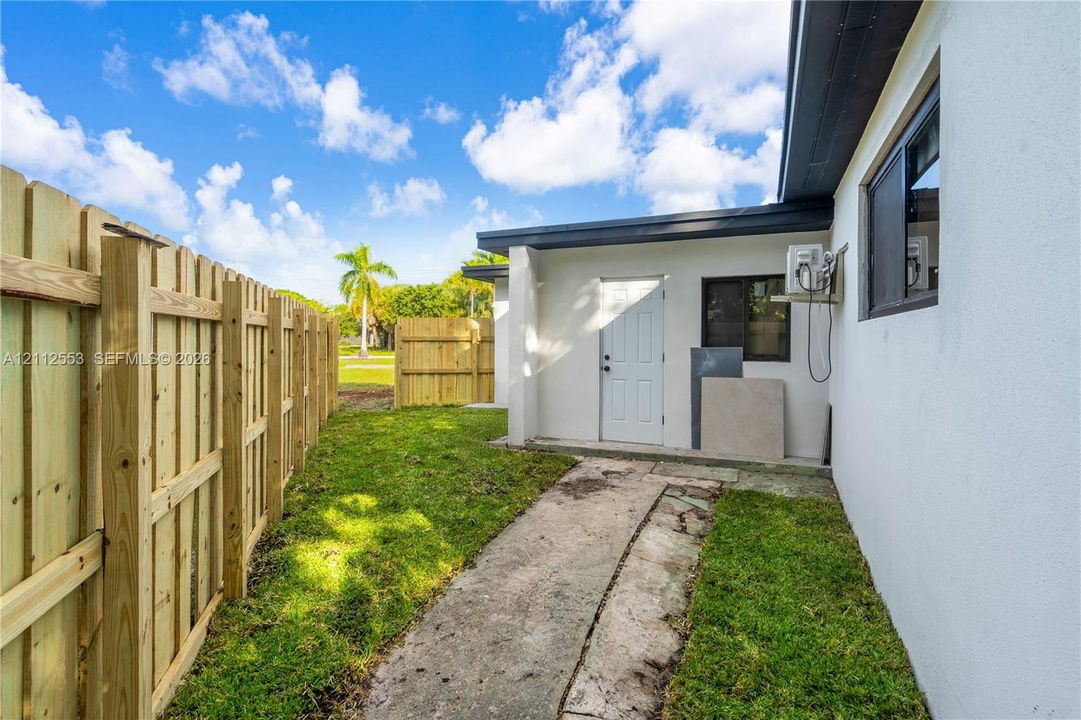 Stucco exterior wall with a wood privacy fence, concrete walkway, and window with dark trim