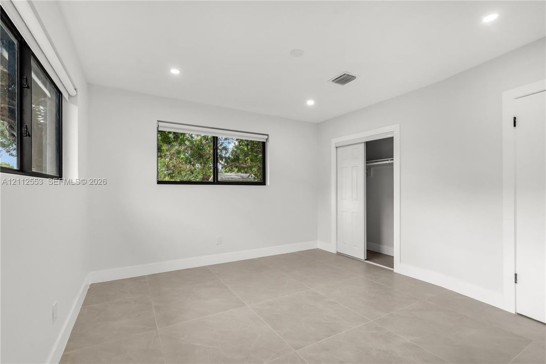 Neutral-toned tile flooring, recessed ceiling lighting, and sliding-door closet featuring a built-in rod