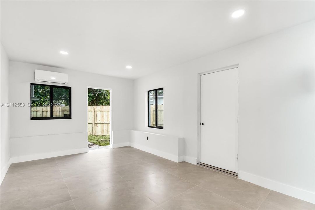 Interior space featuring large-format tile flooring, recessed lighting, dual-pane windows with black frames, and a wall-mounted ductless climate control unit
