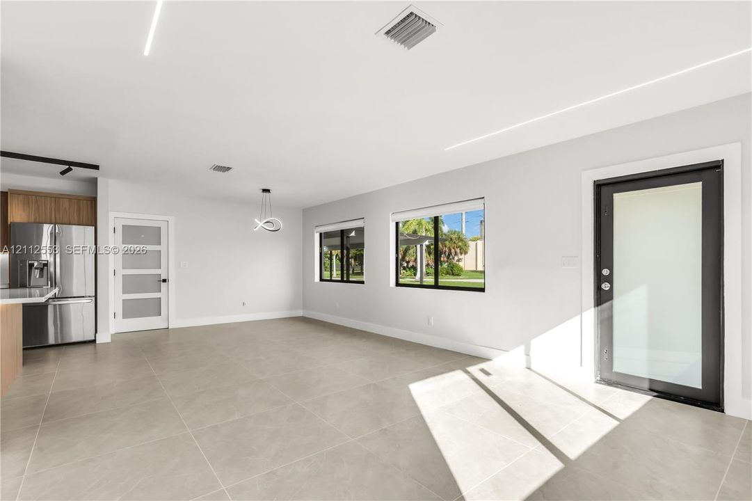 Open-concept interior featuring large-format tile flooring, modern linear recessed lighting, a stainless steel refrigerator, and a contemporary entry door with a glass pane