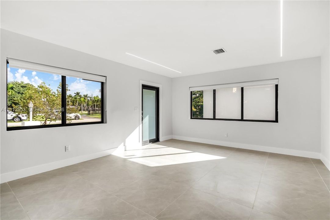 Interior space featuring large-format tile flooring, recessed linear ceiling lighting, black-framed windows with integrated shades, and a glass-paneled exterior door
