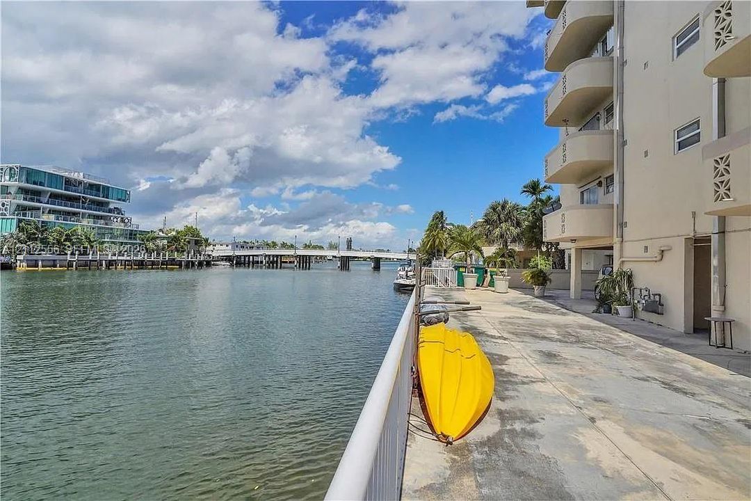 Waterfront concrete patio featuring a metal railing, multi-level balconies, and direct water access