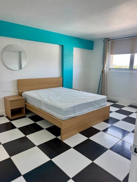 Room featuring black and white checkerboard tile flooring, a circular wall-mounted mirror, and an accent wall painted in a vibrant teal tone