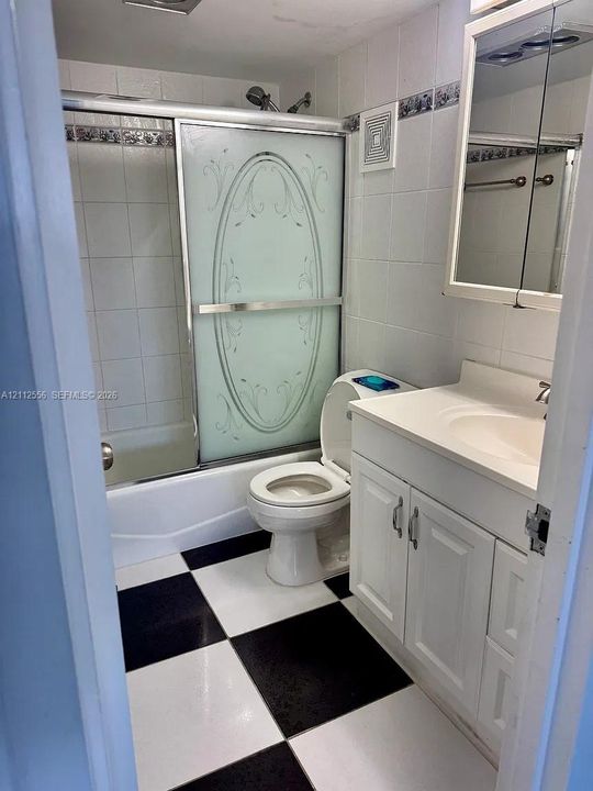 Bathroom featuring a vanity with integrated sink, glass-enclosed shower and tub combination, decorative tile backsplash, and high-contrast checkered flooring