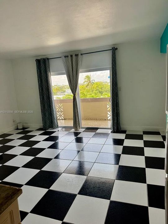 Room featuring a black and white checkerboard tile floor and a sliding glass door with access to a balcony with decorative screen block railings