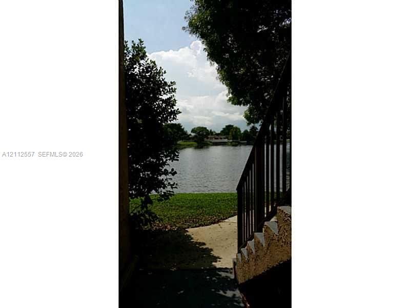 Exterior staircase with metal railings leading to a waterfront lot featuring a grass lawn and mature trees