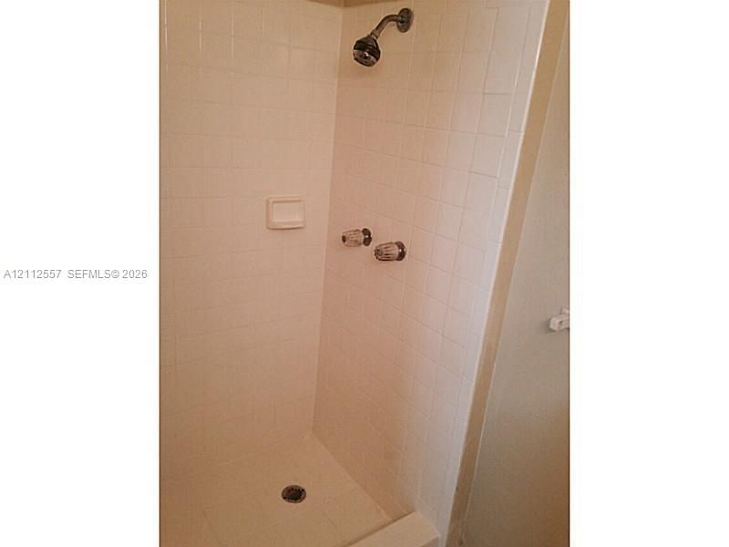 Shower enclosure featuring white square wall tile, a built-in recessed soap dish, chrome dual-handle plumbing fixtures, and a chrome shower head
