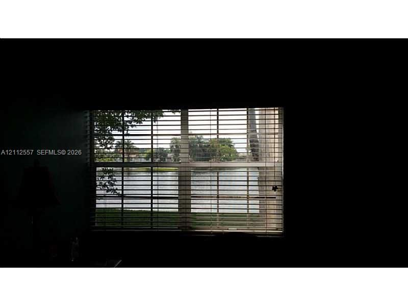 Horizontal slat blinds covering a window providing water frontage and exterior foliage