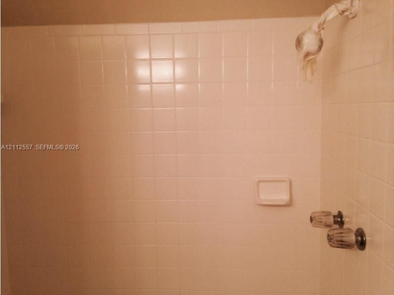 Shower stall featuring white square tile surround, built-in soap dish, and wall-mounted shower head with dual-handle controls