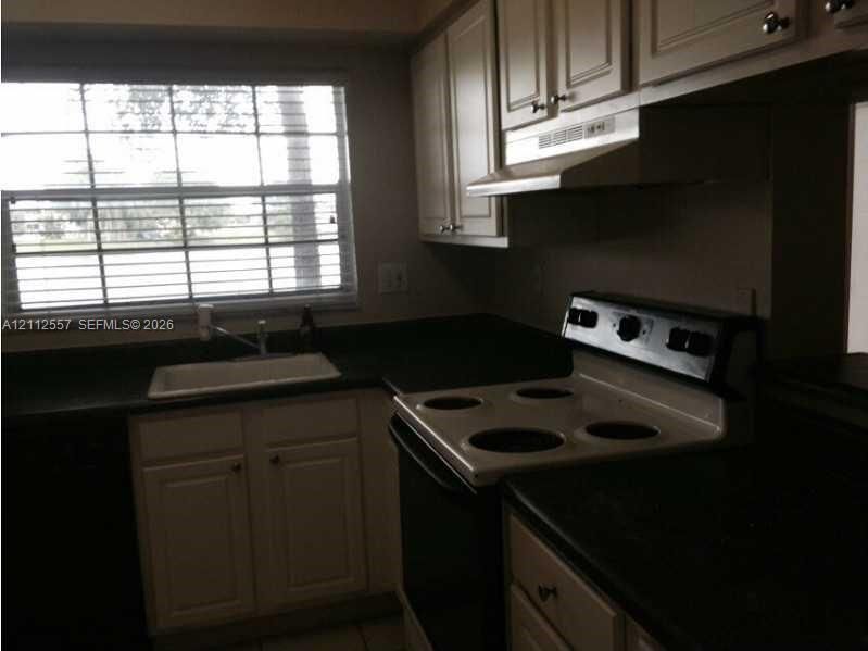 Kitchen featuring cabinetry with crown molding, solid-surface countertops, integrated range hood, white drop-in sink, and large multi-pane window