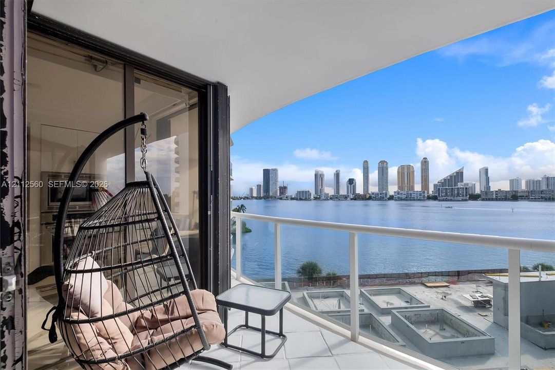 Covered balcony featuring white railings, tiled flooring, and sliding glass door access, highlighting water and city skyline scenery
