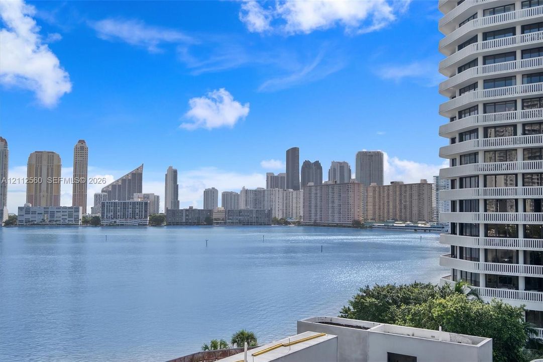 Expansive balcony featuring white railings, overlooking a large body of water and a metropolitan skyline