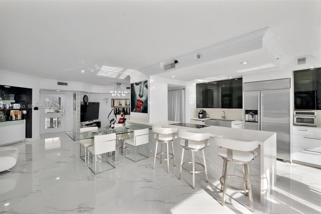 Open-concept kitchen and living area featuring high-gloss cabinetry, stone-finish countertops, stainless steel appliances, and large-format polished flooring