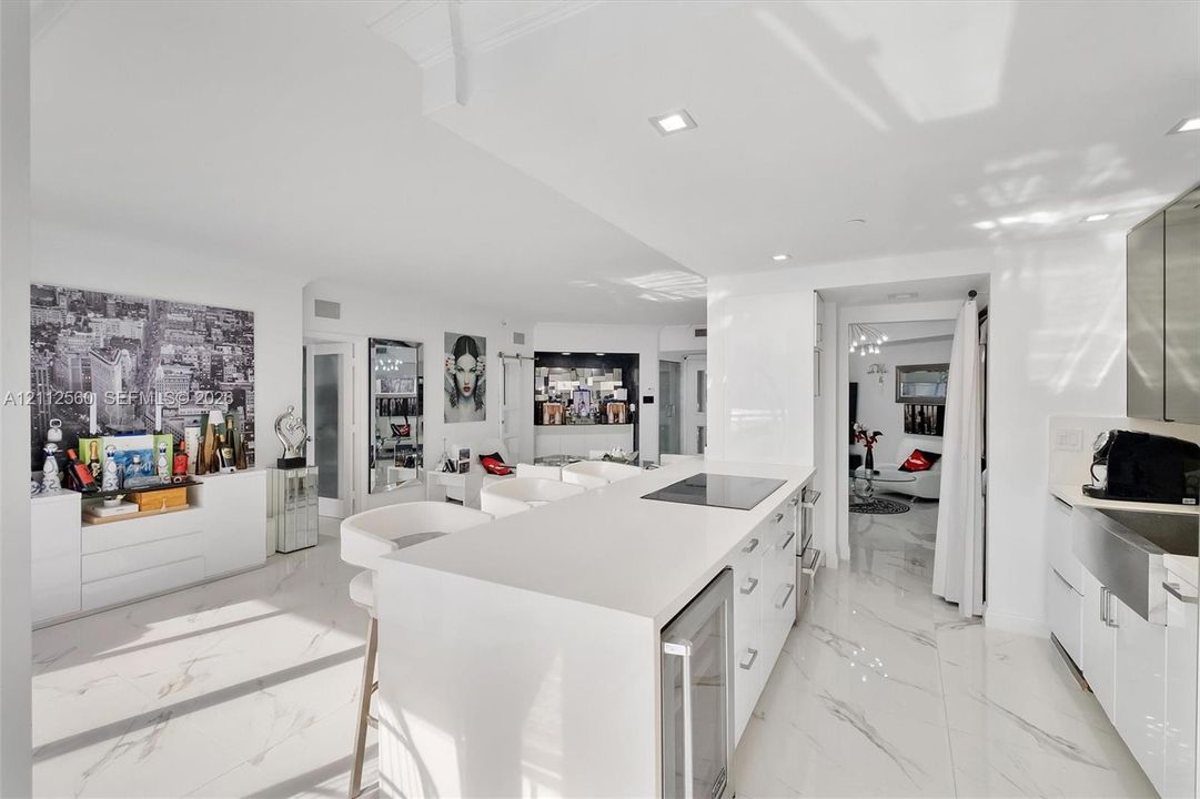 Kitchen featuring a central island with a solid-surface countertop, an integrated electric cooktop, and an under-counter wine refrigerator, complemented by stone-finish flooring and a stainless steel farmhouse-style sink