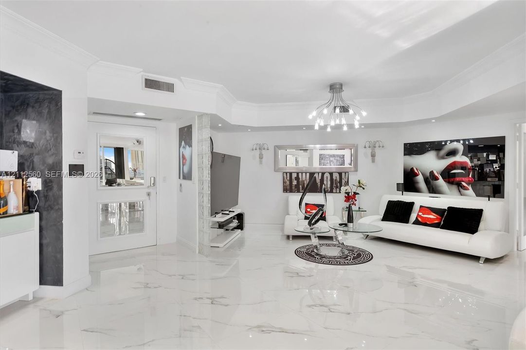 Open living space featuring high-gloss large-format flooring, custom multi-arm chandelier, decorative glass block wall accent, and recessed ceiling lighting