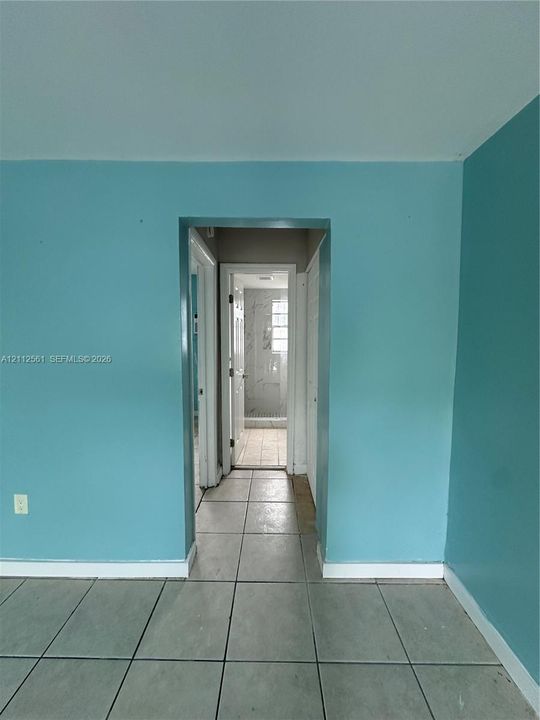 Square tile flooring with a visible doorway leading to a tiled shower enclosure