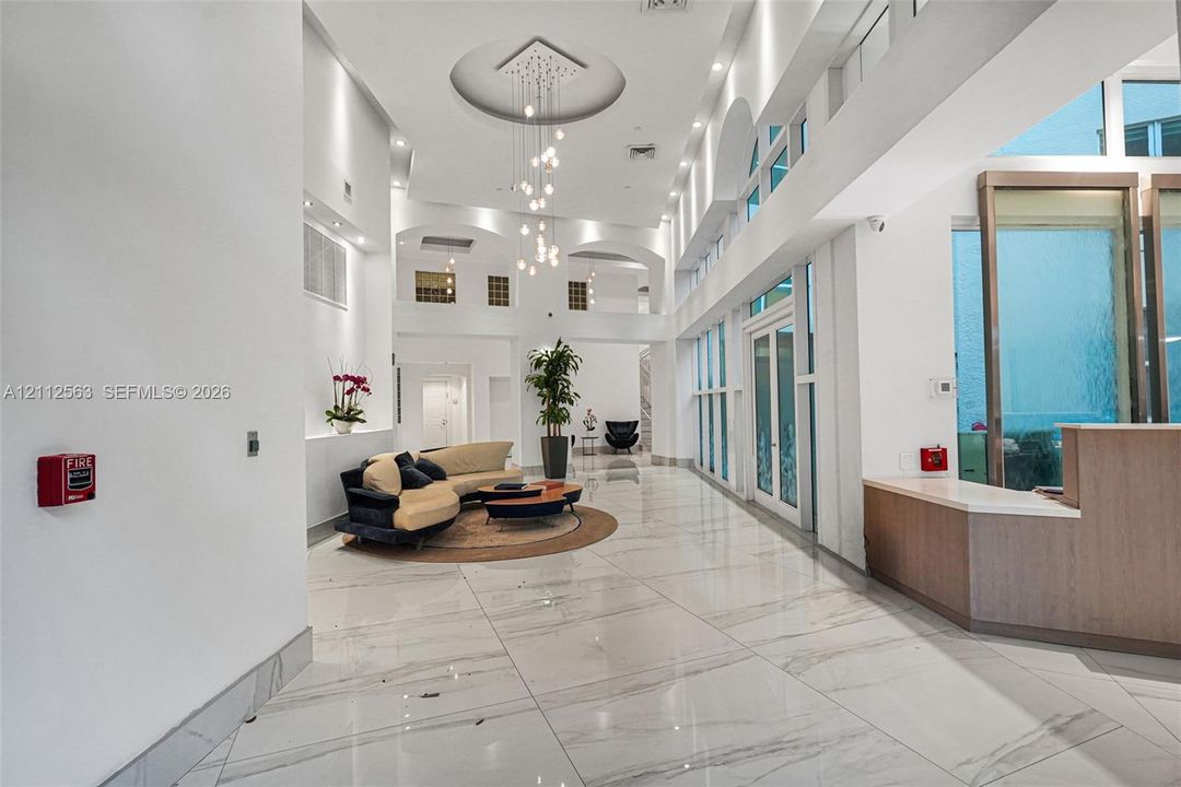 Grand foyer featuring double-height ceilings, stone-finish flooring, floor-to-ceiling windows, arched architectural details, and a tiered modern chandelier