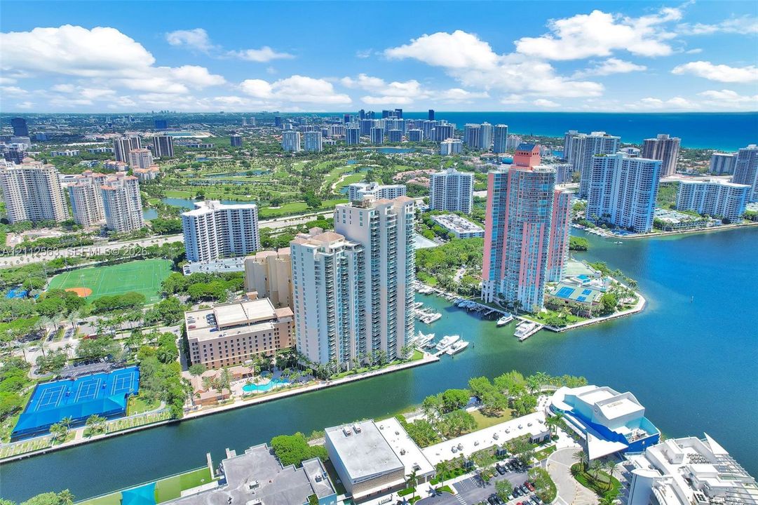 Aerial perspective featuring a waterfront high-rise development, a deep-water marina, proximity to coastal waterways, and urban skyline surroundings