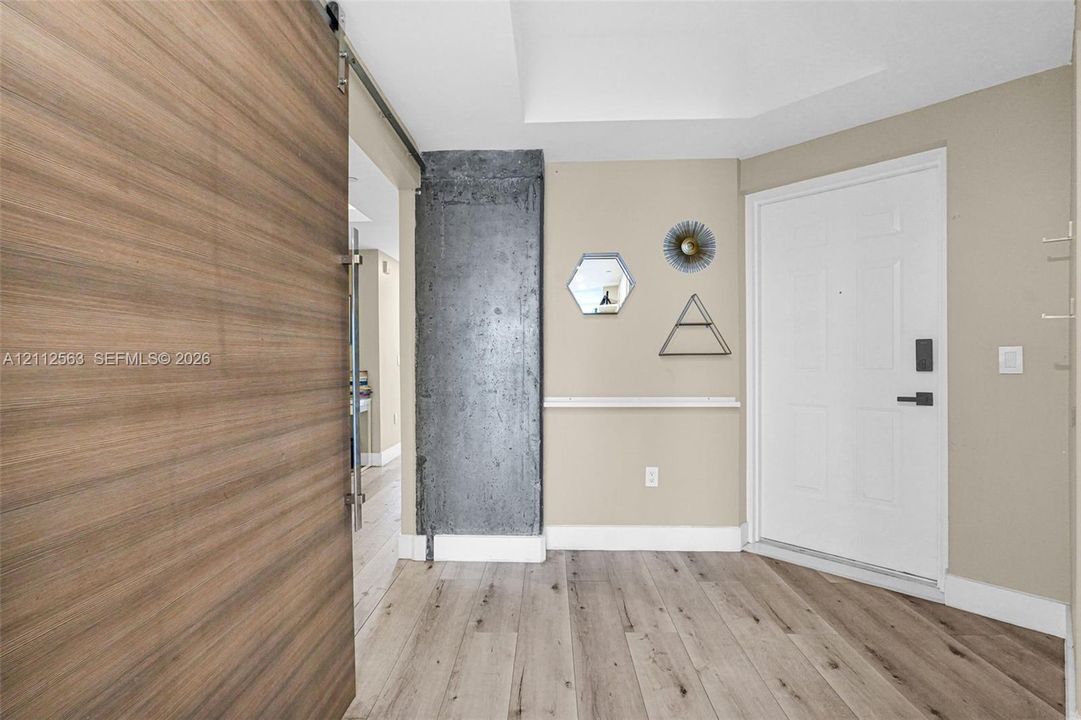 Entryway featuring wood-finish flooring, a sliding wood-finish barn door, an exposed concrete pillar, and a white panel door with integrated electronic lock