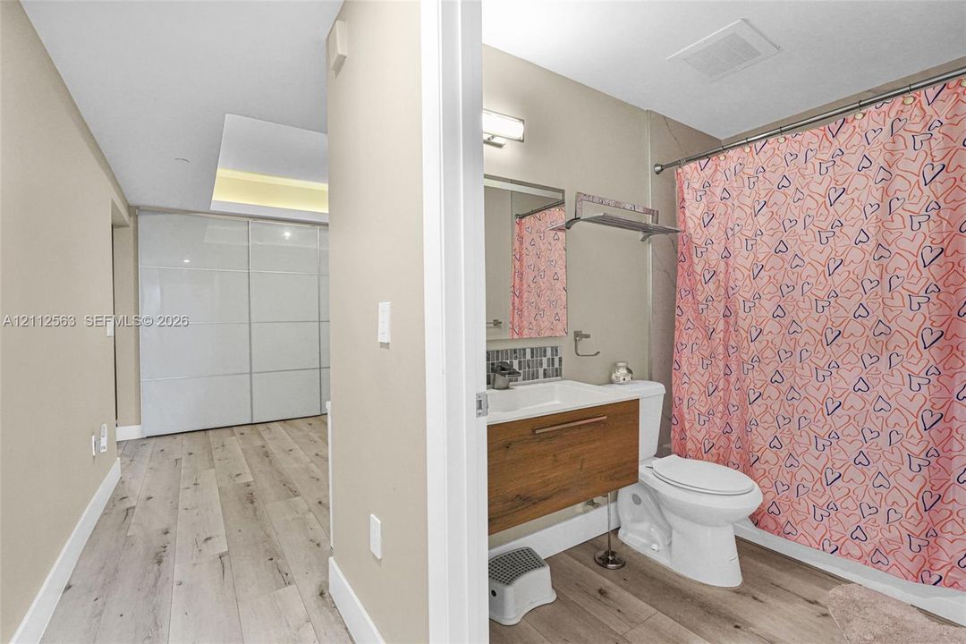 Bathroom featuring a wood-finish floating vanity, integrated sink, tiled backsplash, and recessed lighting, with wood-finish flooring extending into the area