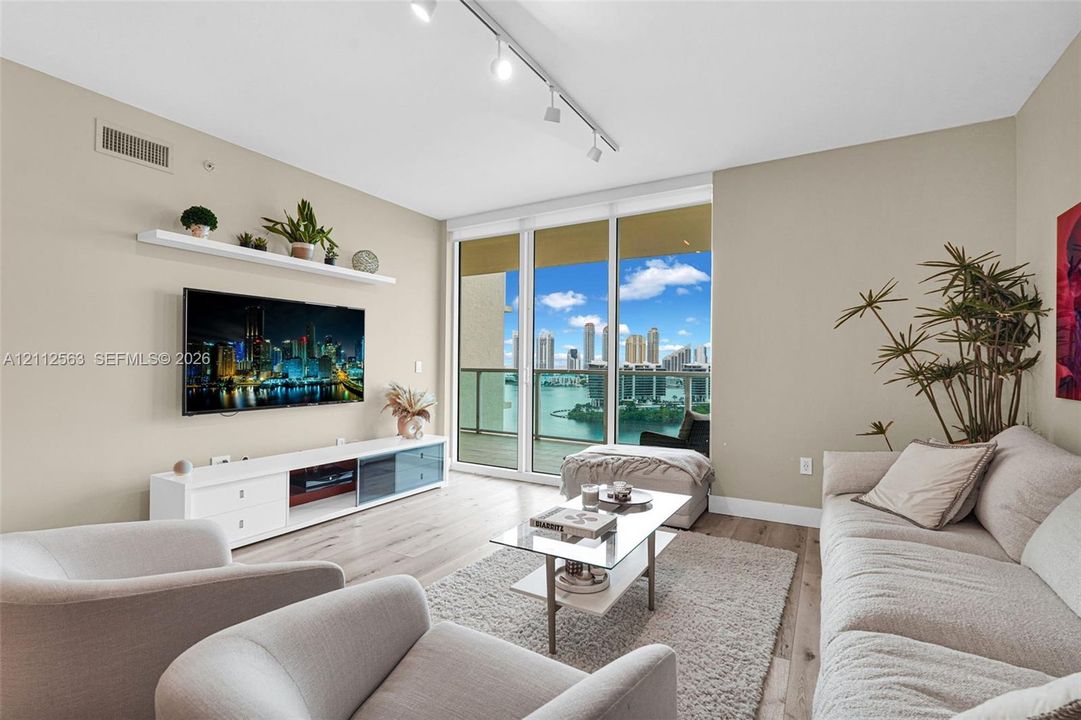 Living area featuring wood-finish flooring, floor-to-ceiling glass doors, built-in wall shelving, track lighting, and a private balcony