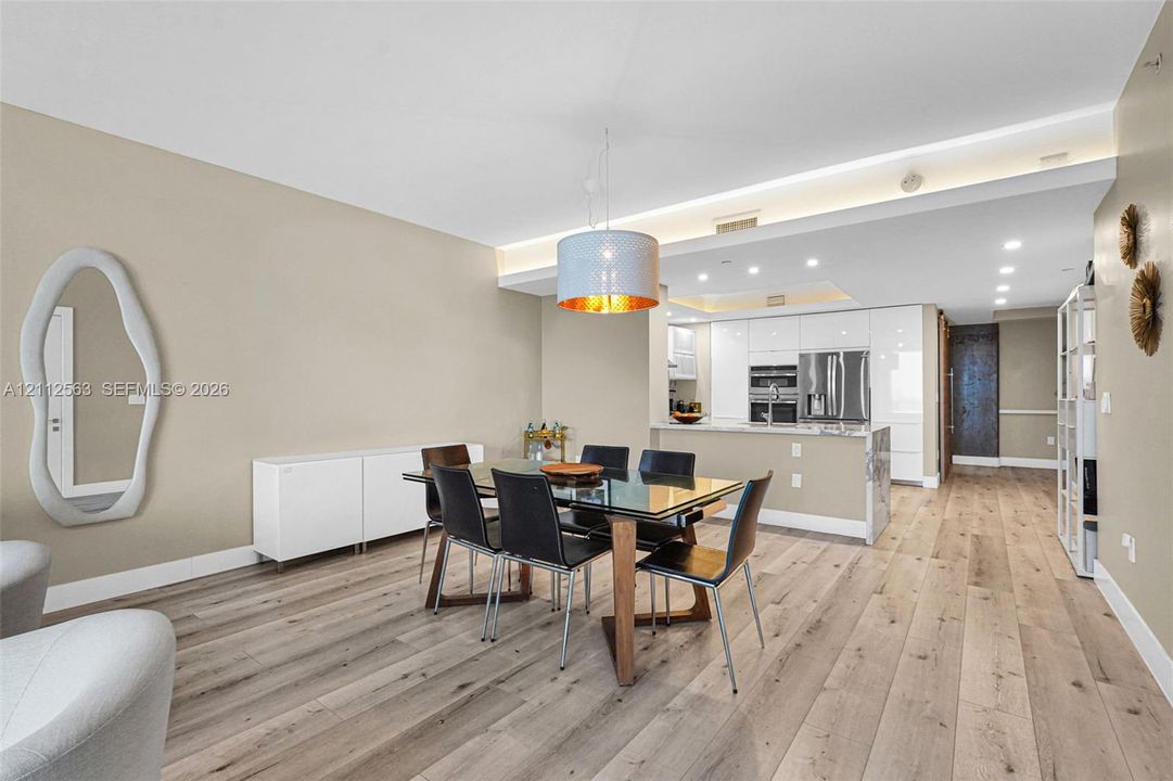 Open-concept interior featuring light wood-finish flooring, recessed ceiling lighting, a contemporary pendant light fixture, and high-gloss white cabinetry