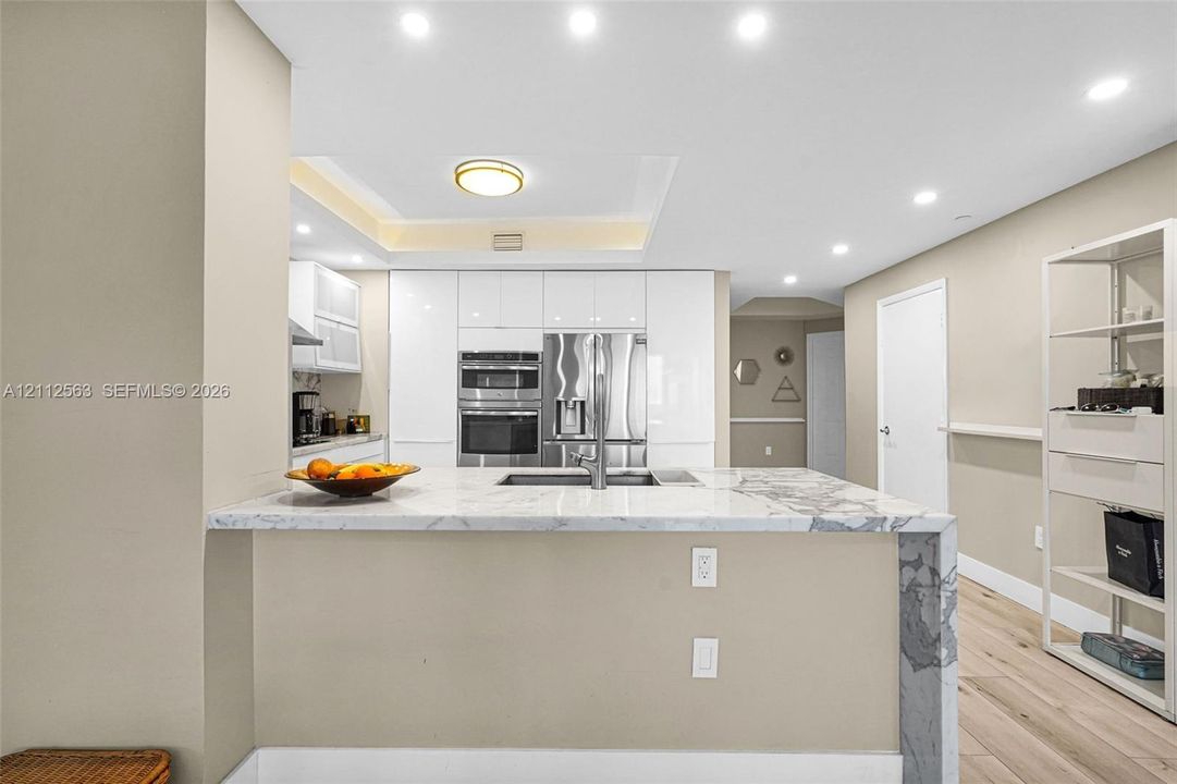 Kitchen featuring white slab-front cabinetry, a waterfall-edge stone island, integrated stainless steel appliances, recessed lighting, and wood-finish flooring