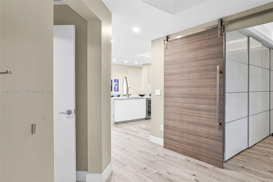 Wood-finish sliding barn door featuring a stainless steel track system and handle, wide-plank wood-finish flooring, and recessed ceiling lighting