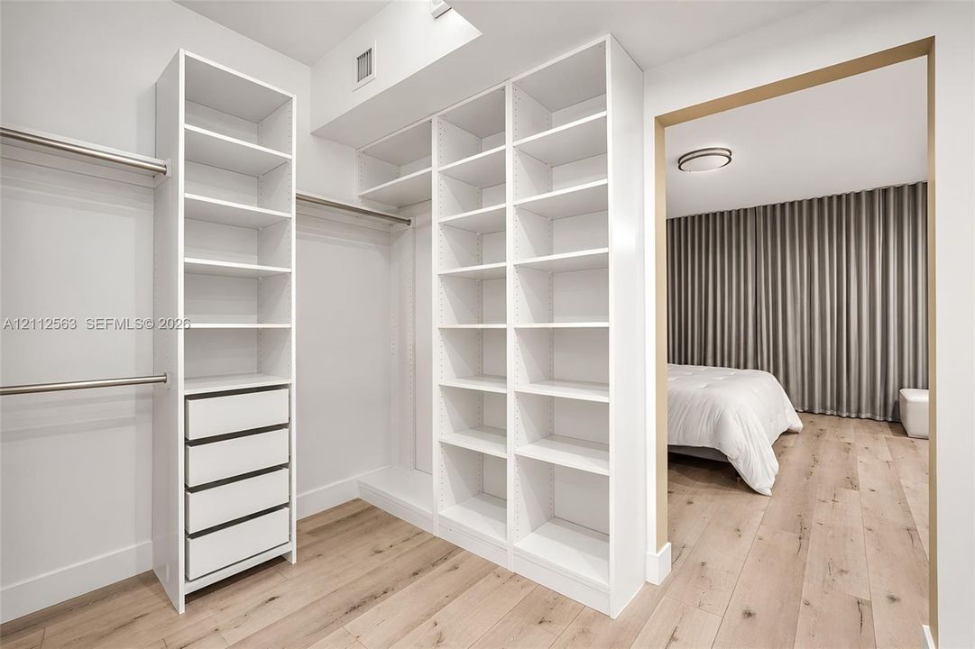 Custom walk-in closet featuring white built-in shelving, integrated drawers, metal hanging rods, and wood-finish flooring