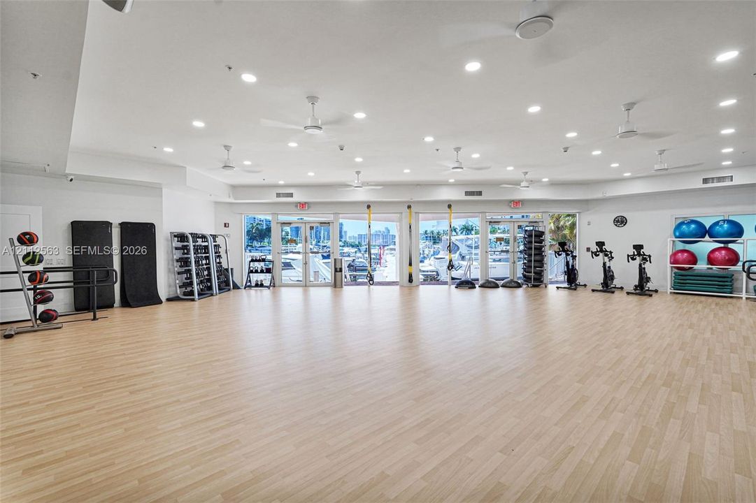 Fitness room featuring wood-finish flooring, recessed lighting, multiple ceiling fans, and full-height glass-paneled entry doors