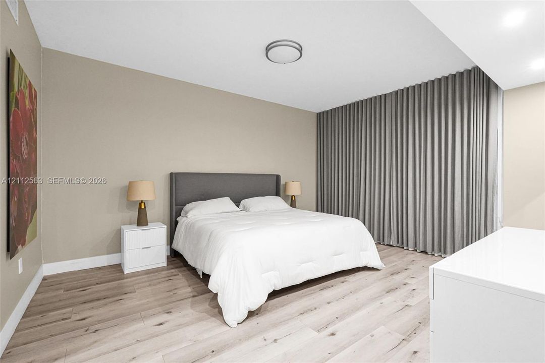 Neutral-toned interior featuring wood-finish flooring, floor-to-ceiling pleated drapery, and flush-mount ceiling lighting
