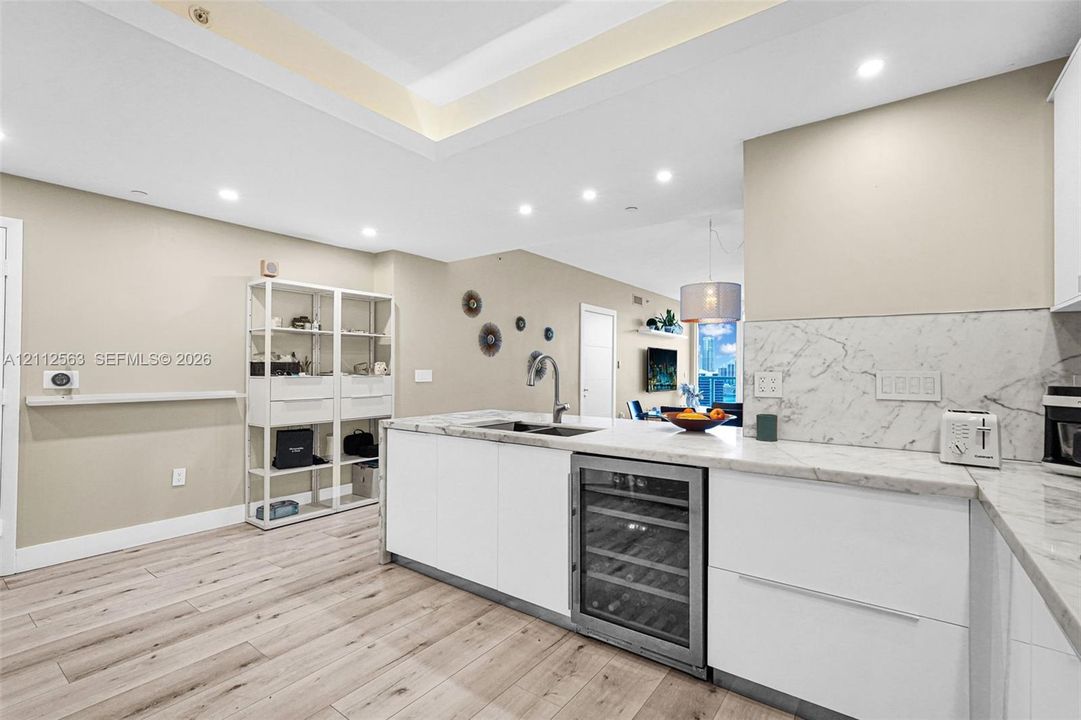 Kitchen featuring an island with stone countertops, a built-in wine refrigerator, recessed ceiling lighting, and wood-finish flooring
