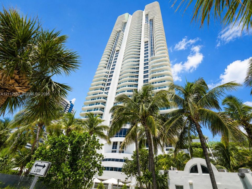 High-rise building featuring curved white balconies, floor-to-ceiling glass windows, and exterior palm landscaping