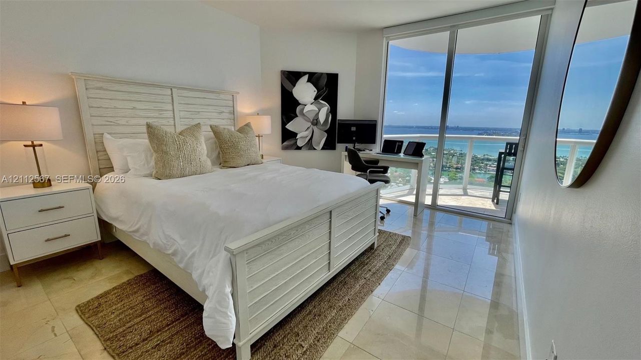 Floor-to-ceiling sliding glass doors, polished stone flooring, and expansive wrap-around balcony with coastal scenery