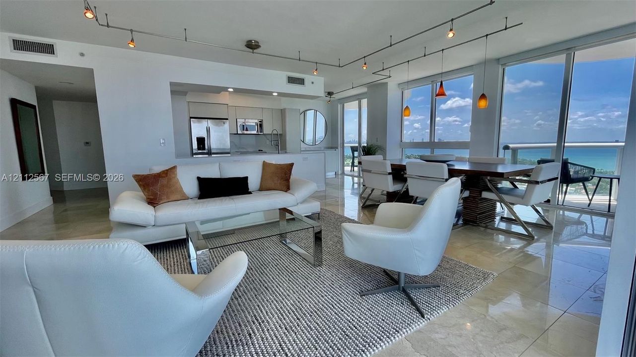 Open-concept living space featuring floor-to-ceiling windows, polished stone flooring, custom track lighting, and built-in kitchen cabinetry