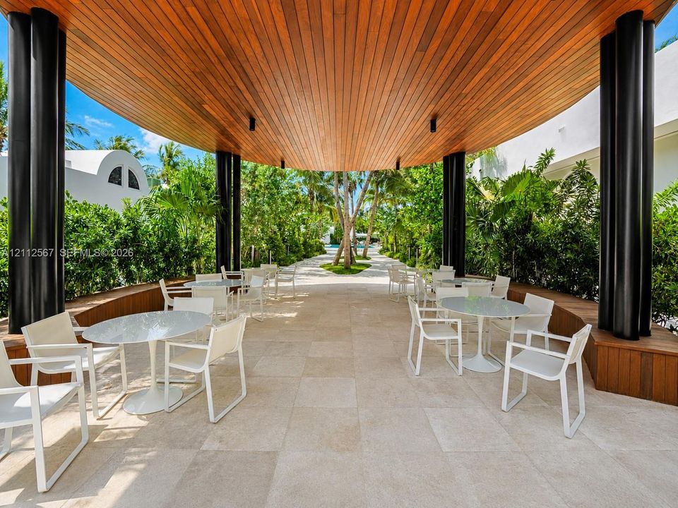 Covered outdoor patio featuring a vaulted wood-slat ceiling, structural cylindrical pillars, built-in wooden bench seating, and natural stone tile flooring