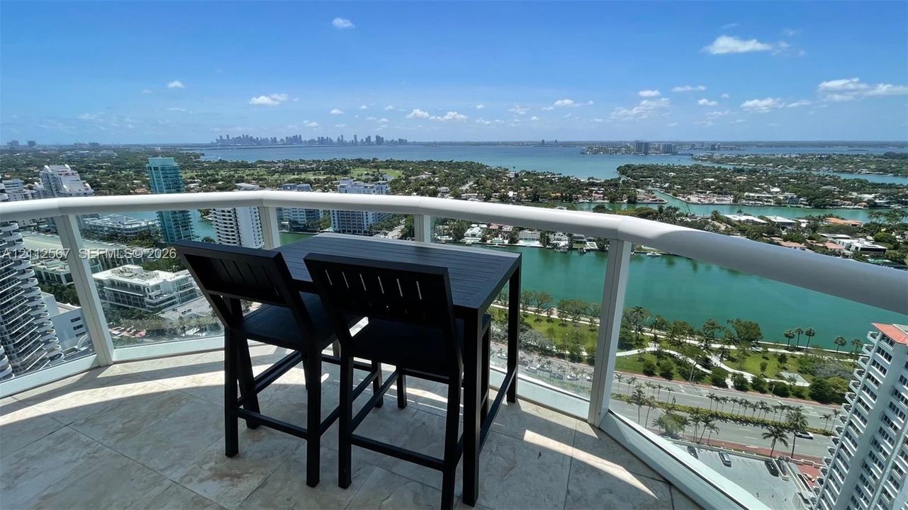 Covered balcony featuring stone tile flooring and a curved white railing