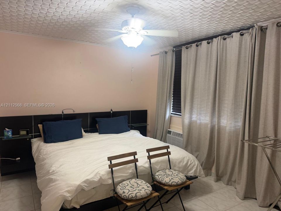 Textured ceiling, tile flooring, built-in black headboard with integrated shelving, and ceiling fan with integrated lighting