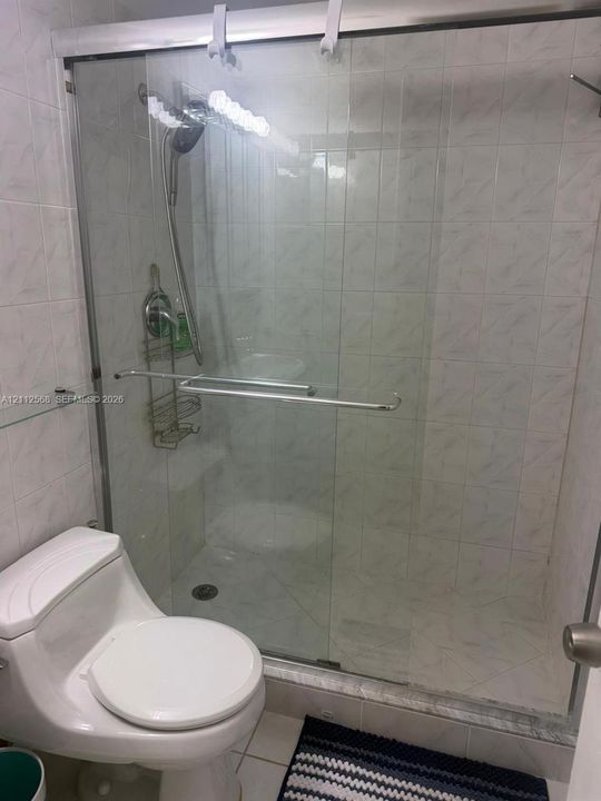 Walk-in shower enclosure with glass sliding doors, chrome hardware, adjustable handheld shower fixture, and floor-to-ceiling tile surround