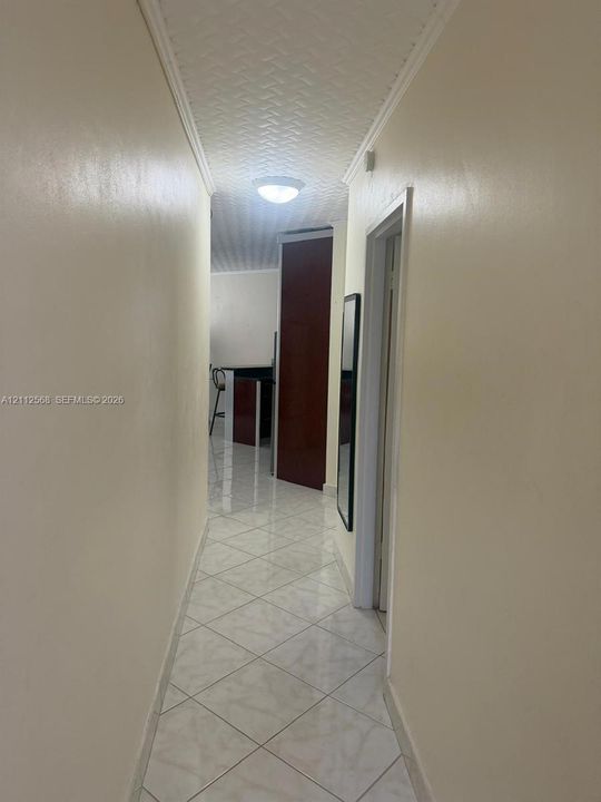 Hallway featuring neutral wall tones, large-format diamond-pattern floor tiles, and a textured ceiling finish with a flush-mount light fixture