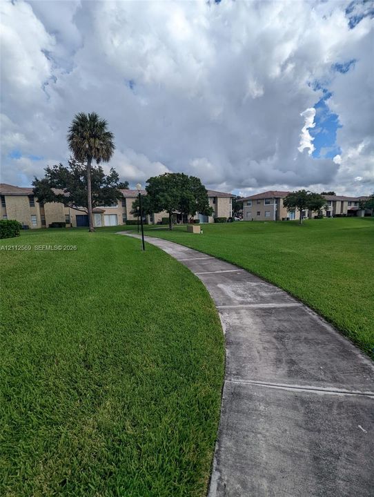 Expansive green space featuring a concrete pathway, mature trees, and multi-story structures with masonry facades