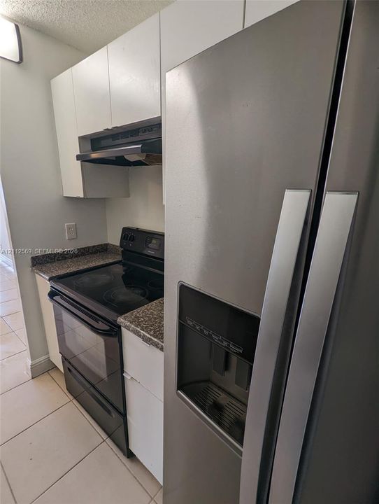 Kitchen featuring flat-panel white cabinetry, speckled stone-finish countertops, black electric range, integrated range hood, and stainless steel side-by-side refrigerator
